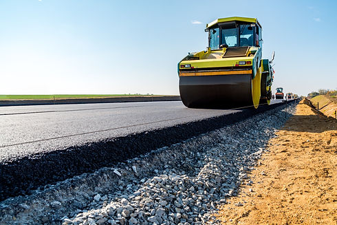 A large yellow steamroller paving a new road, compacting fresh asphalt