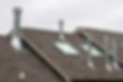 Sloped rooftop with gray shingles, featuring multiple metal chimneys and two skylights