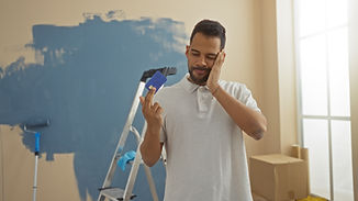Young man in new home looks worried with credit card amidst unpacking and painting