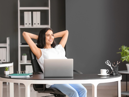 A young woman sits at her desk in an office with a relaxed expression.