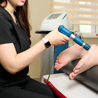 A therapist performs shockwave therapy on a patient's foot using a handheld device