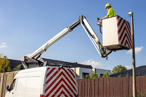 A worker in a bright yellow vest and hard hat operates a bucket lift