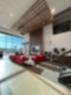 Spacious modern waiting area with red sofas, a TV, large windows, and a coffee station