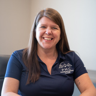 A woman with long dark hair sitting at a desk with a navy shirt and white background.