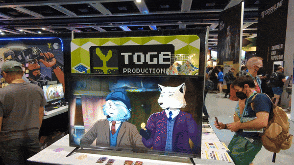 A GIF showing Toge Productions' booth at PAX West. Slowly panning from right to left, you can see a trailer for Moses and Plato playing on a TV, a big banner for the company hung against the wall they've built behind that, and various stations for each of their games. Coffee Talk Episode 2, A Space for the Unbound, Whisper Mountain Outbreak, and more. VGG's Editor-in-Chief can be seen playing a game and talking to someone at the booth.