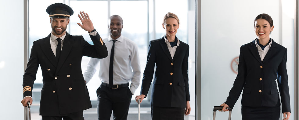 Flight crew walking in an airport with suitcases smiling and waving.