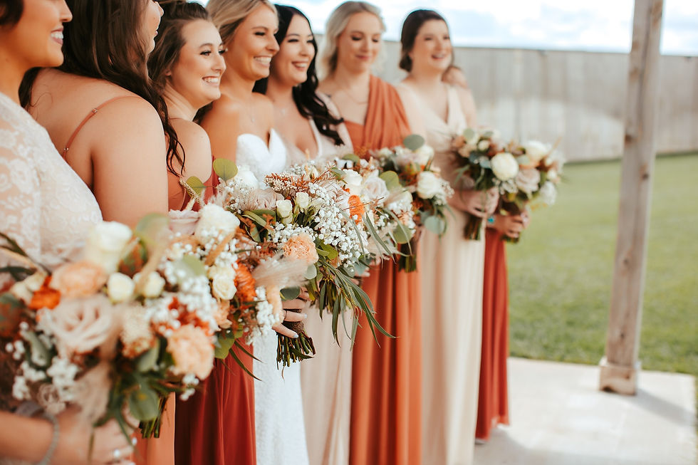 Smiling bridesmaids in terra cotta, peach and cream dresses hold floral bouquets at an outdoor wedding ceremony in the Texas Panhandle. 