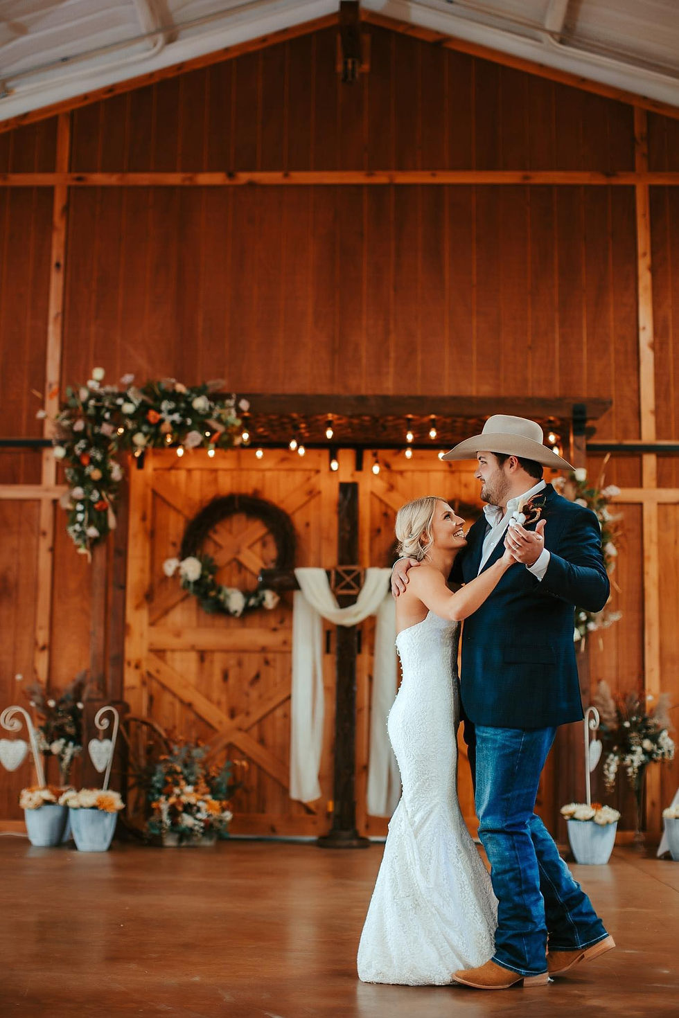 dim lit ambiance surround the newlyweds as they share their first dance as husband and wife in rustic elegant wedding venue near amarillo texas, elegant barn venue near amarillo, fresh florals draped on pergola with old fashioned lights, cowboy groom with cowboy hat and boots dance the night away on our open dance floor