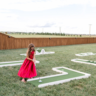 Flower girl plays mini golf yard games at Amarillo wedding venue during cocktail hour at wedding.