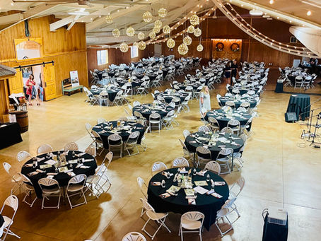 Large indoor event space in Amarillo with round tables, black tablecloths, centerpieces, and soft overhead string lights