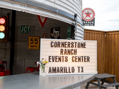 Silo Bar with red stools and a metal countertop. Sign reads "Cornerstone Ranch Events Center Amarillo TX." Traffic signs and lights in background.
