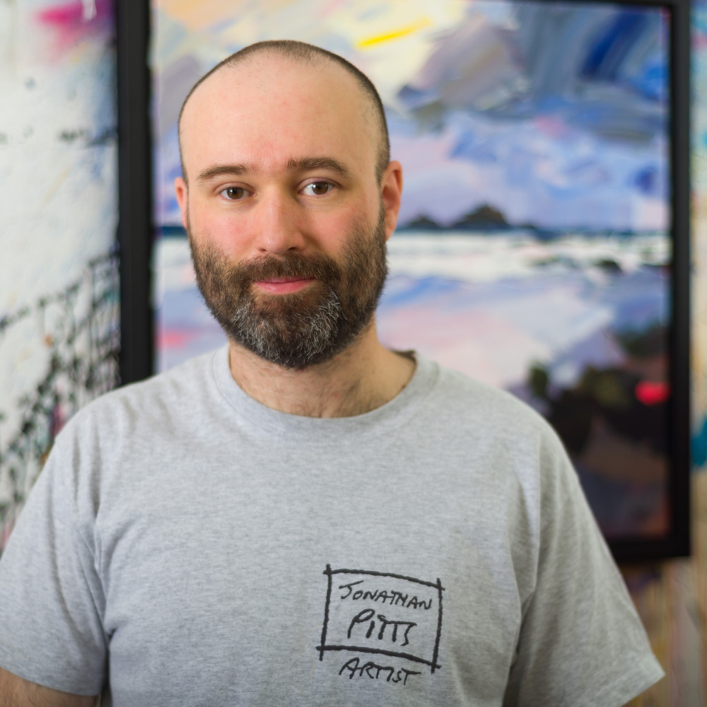 Jonathan Pitts artist sat in front of an acrylic painting on canvas of the Brisons in Cape Cornwall