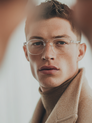 Close-up of person with red hair, clear glasses, and brown turtleneck looking at camera.
