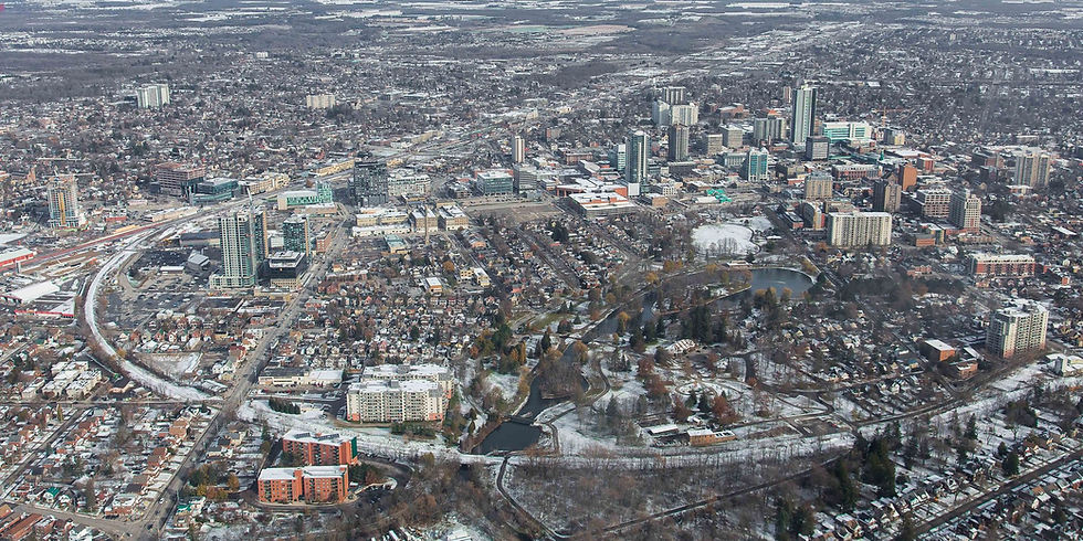 Aerial winter view of a snowy city skyline with parks, ponds, and dense neighborhoods under a gray sky.