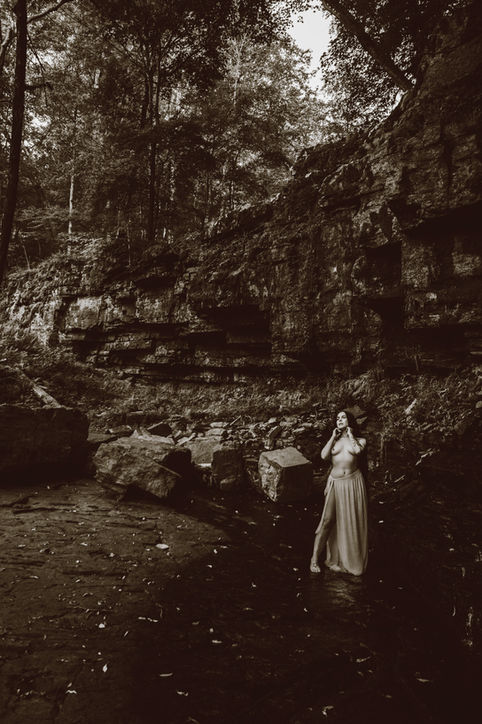 A woman poses dramatically in front of a large rock wall and trickling waterfall. Fine art nature portrait photography, New Hope, Bucks County, PA, Lexi Bird Photography