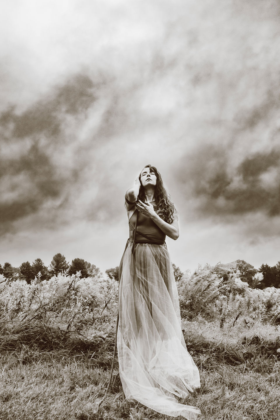 A woman stands in a field with a dramatic skyline behind her. The mood is dark and emotional. Creative fine art portraits, Greater Philadelphia, PA, Lexi Bird Photography