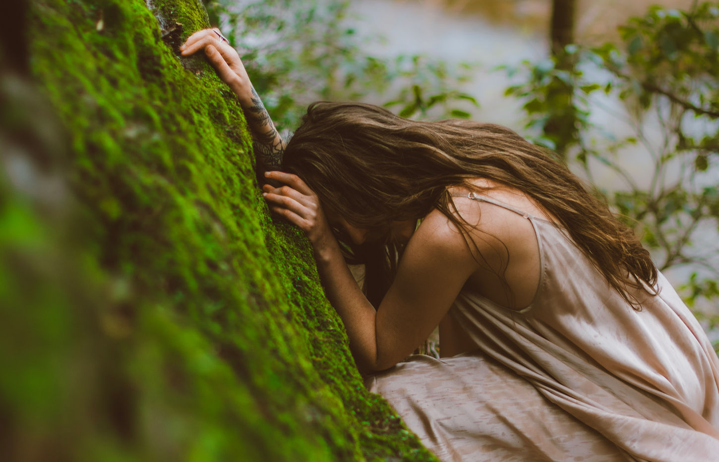 Woman curled up and leaning against a mossy rock with her face concealed — fine art outdoor portrait by Lexi Bird Photography, Bucks County PA
