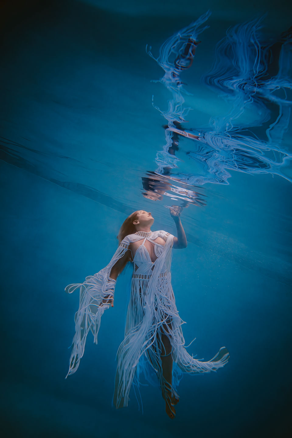 Woman in white dress with long tassels made by Altysan Wearable Art floats underwater near the surface. Underwater photographer, Bucks County, PA, Lexi Bird Photography