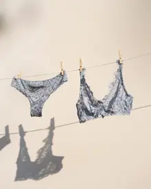 Sky blue lace lingerie set hanging on a clothesline with shadows on a white wall