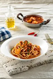 Plate of spaghetti with seafood sauce, garnished with chili and parsley, on a rustic table with olive oil in the background