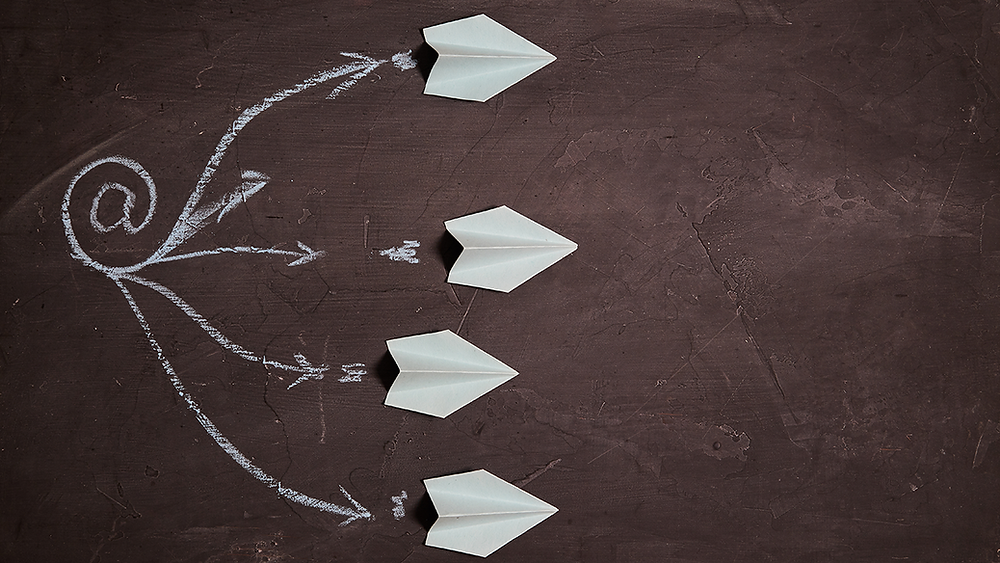 An @ symbol on a chalkboard with lots of paper airplanes surrounding it