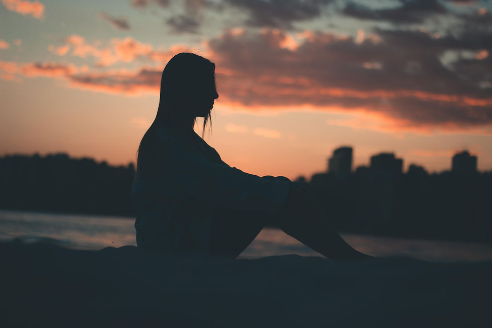 Silhouette of a person sitting alone at sunset by the water, reflecting quietly, symbolizing grief, loss, and emotional healing.