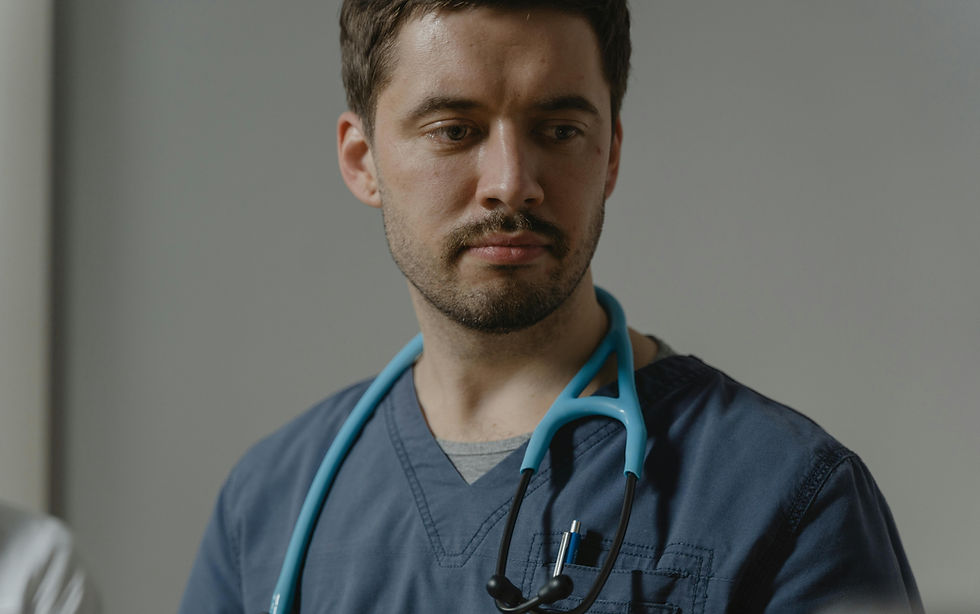 A veterinary professional in scrubs looks off thoughtfully with a calm, reflective expression, representing the emotional weight, compassion, and quiet resilience involved in veterinary care.