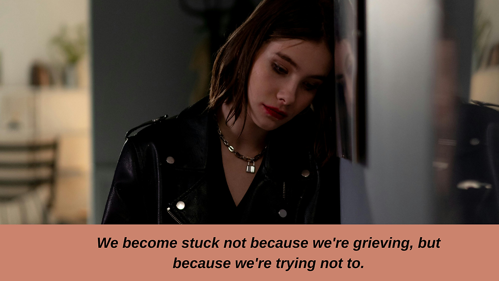 Woman in black jacket leans against a wall, looking sad. Text below reads: "We become stuck not because we're grieving, but because we're trying not to."