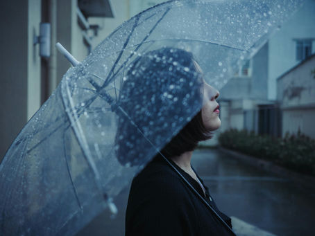 Person standing under an umbrella in the rain, looking upward, symbolizing emotional overwhelm, stress, and feeling caught in a cycle of self-pressure.