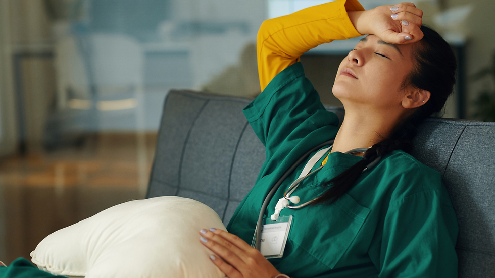 A veterinary professional in scrubs sits on a couch with eyes closed and hand on her forehead, reflecting emotional exhaustion, mental overload, and the weight of carrying stress, grief, and responsibility without adequate release.