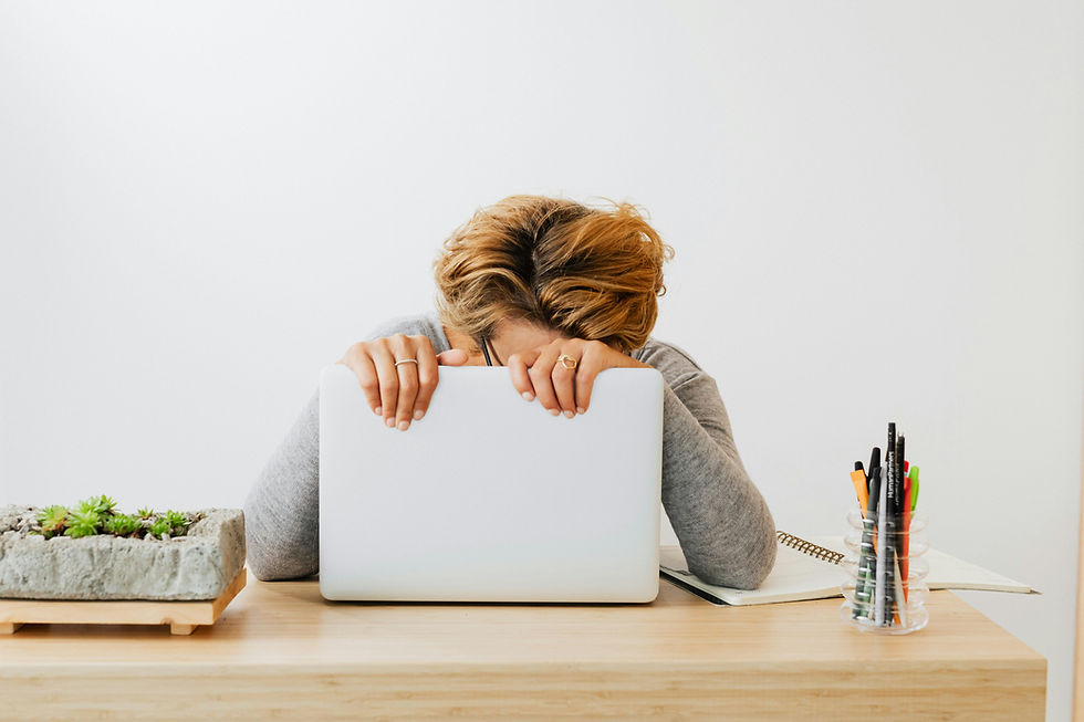 Person resting head on laptop, sitting at a wooden desk with a succulent planter and pens. The setting is minimalistic, conveying fatigue.