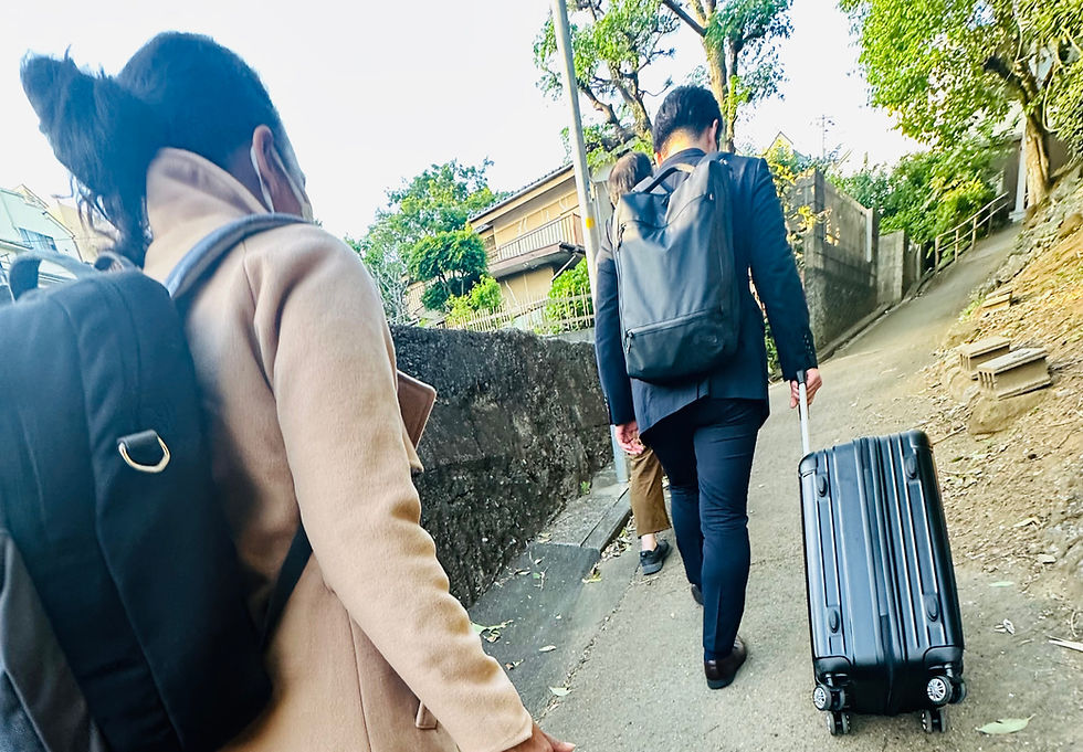 坂道をキャリーケースと大きな荷物を持って移動する特定技能介護インドネシア人材と登録支援機関スタッフ