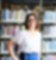 A woman with brown hair and glasses smiling in front of library bookstacks