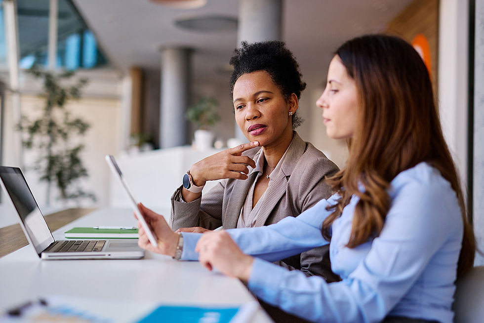 Two female colleagues sit and look at a tablet and laptop