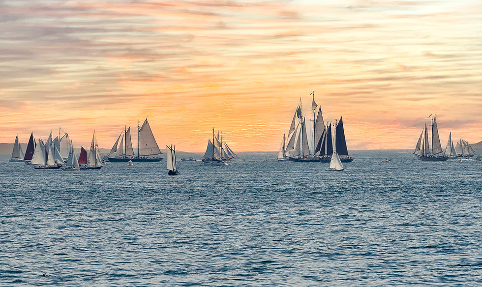 Gloucester Schooner Festival at sunset—historic vessels gather offshore under full sail.