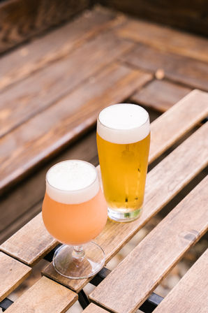 an orange cocktail drink in a cocktail glass next to a glass of beer on top of a wooden table in the backyard of the Doppelgänger Brooklyn Bar