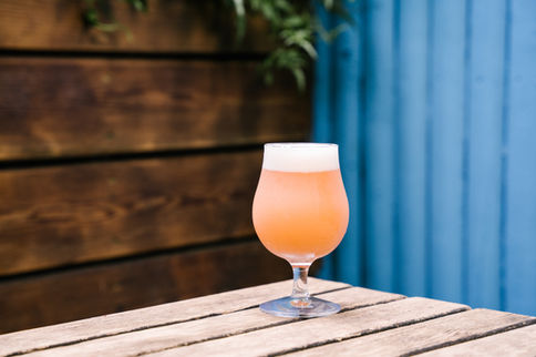 an orange cocktail drink in a cocktail glass on top of a wooden table in the backyard of the Doppelgänger Brooklyn Bar