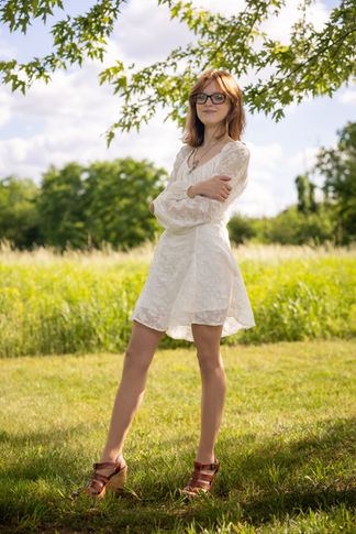 a woman in a white dress and glasses stands in a field