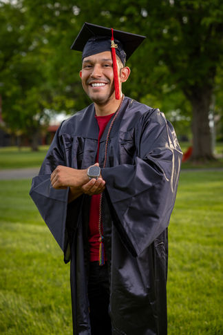 a man in a graduation cap and gown is smiling and holding a watch