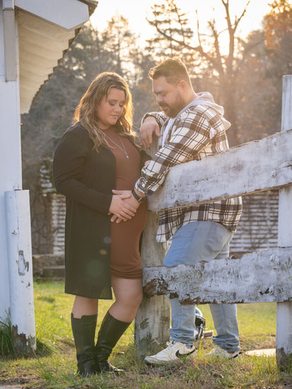 a man and a pregnant woman lean against a wooden fence