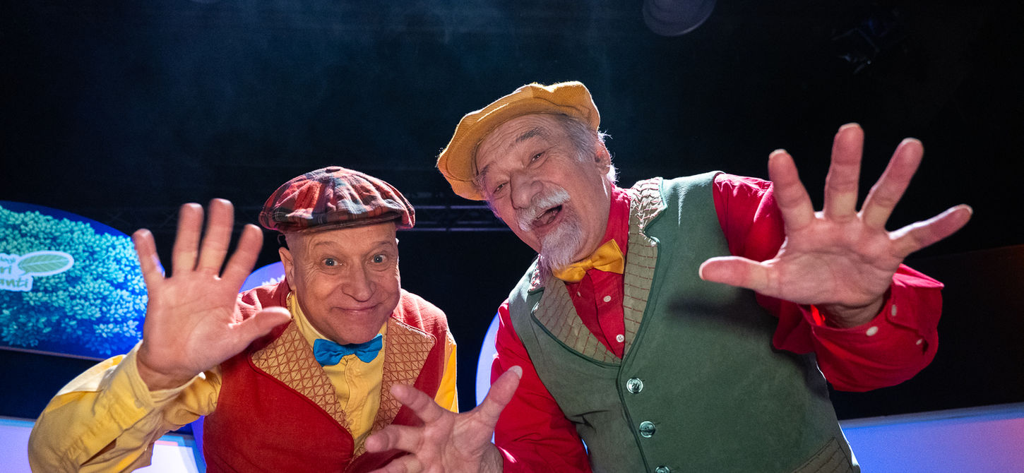 foto di Sergio Manfio e Francesco Manfio con uno sfondo per la metà inferiore illuminato e la metà superiore nera. loro sono sorridenti con le mani aperte. uno spettacolo che andrà in scena al Teatro Bobbio de La Contrada di Trieste