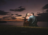 Engaged couple leaning in for a kiss sitting on the grass overlooking the ocean during a twilight engagement portrait photography shoot in Oahu, Hawaii.