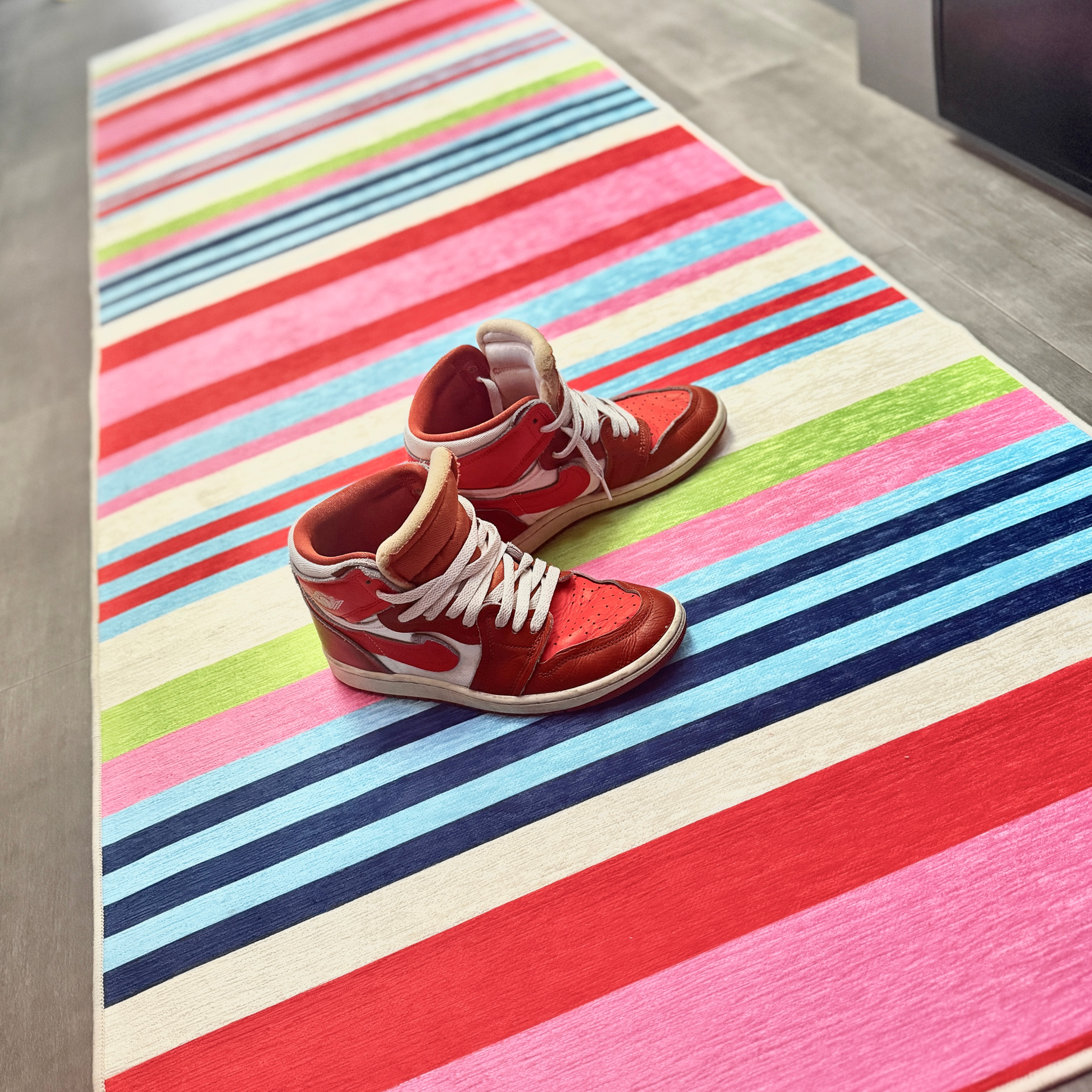 The delightfully stripey washable rug in pink, red, blue, and lime — styled with my red high-tops, because it really pulls the room together.