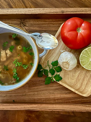 A warm bowl of quick homemade chicken noodle soup served with fresh garlic, lime, tomato, and herbs—simple ingredients that bring comfort when someone in the family isn’t feeling their best.