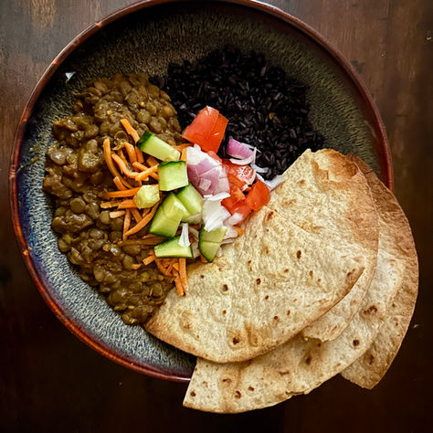 Cozy bowl of Indian masoor dal made with earthy red lentils and warm spices, served with purple rice, fresh vegetable toppings, and soft whole-wheat roti for an easy, comforting, plant-based meal with a little kick.