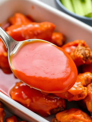 A tantalizing spoonful of our signature buffalo sauce being poured over smoked wings.