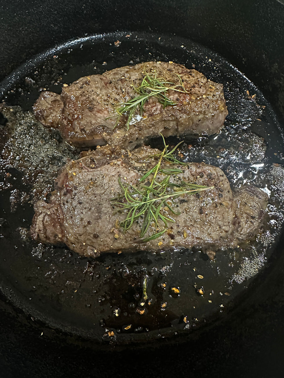 Perfectly seared steaks garnished with fresh rosemary in a sizzling pan.