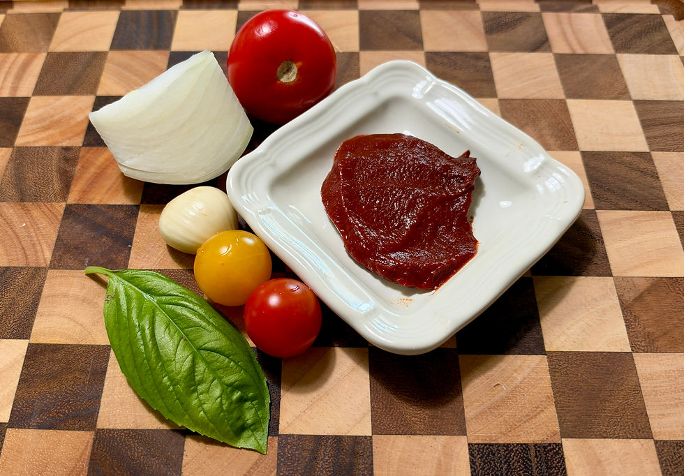 Tomato paste on a white dish with fresh tomatoes, onion, and basil on a wooden cutting board for homemade pasta sauce.