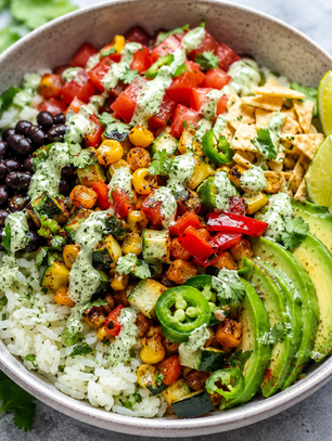 A vibrant and flavorful Spicy Veggie Taco Bowl, adorned with colorful veggies, black beans, ripe avocado slices, and lime wedges, all drizzled with a creamy cilantro lime sauce.