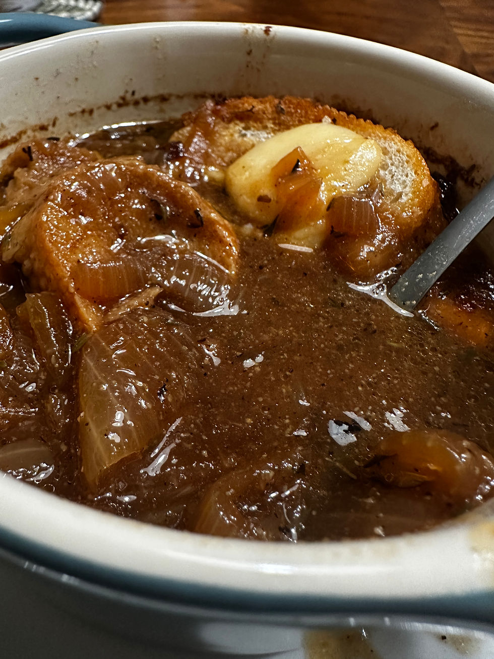 Close-up of homemade French onion soup with caramelized onions, toasted French bread, and melted cheese in a ceramic crock.